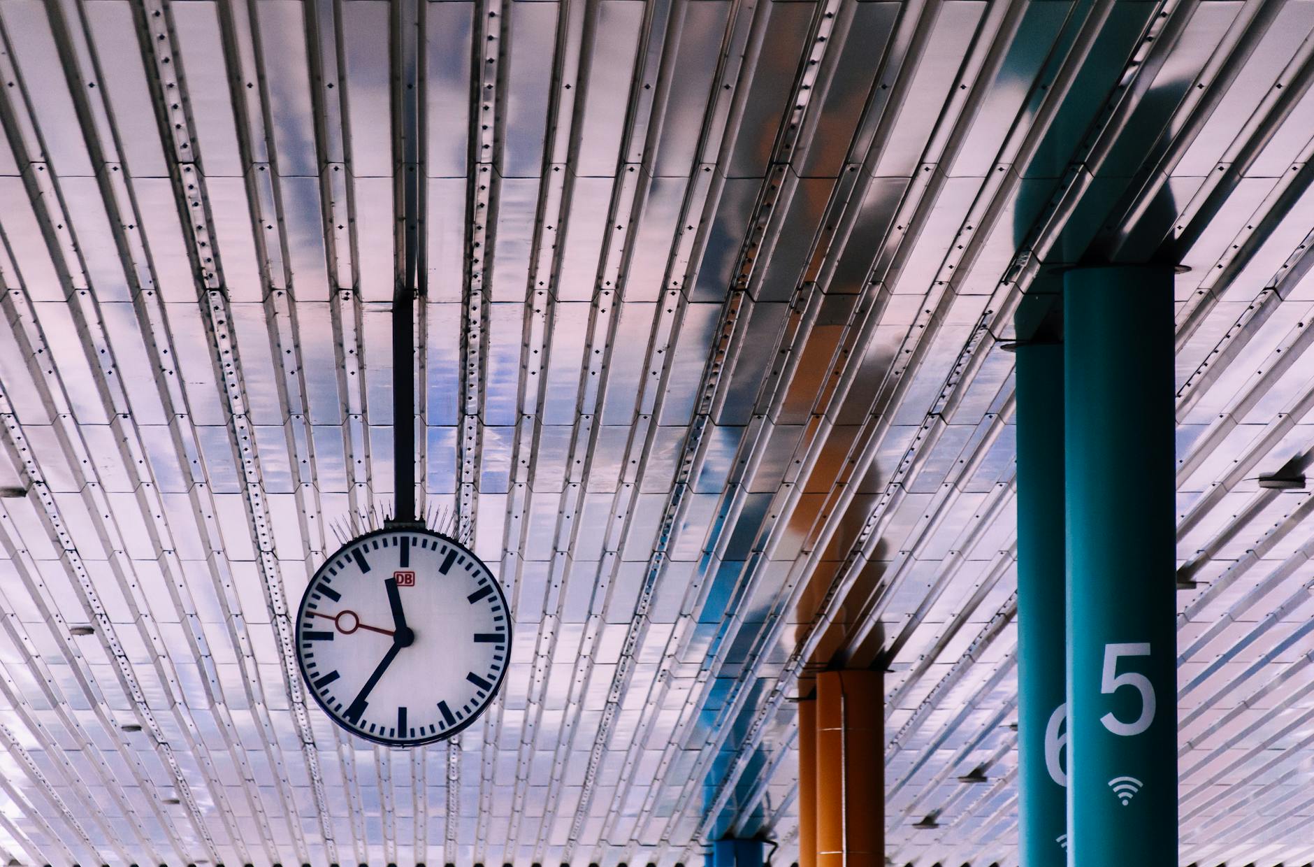 View of a modern train station ceiling with metal panels and a large clock.