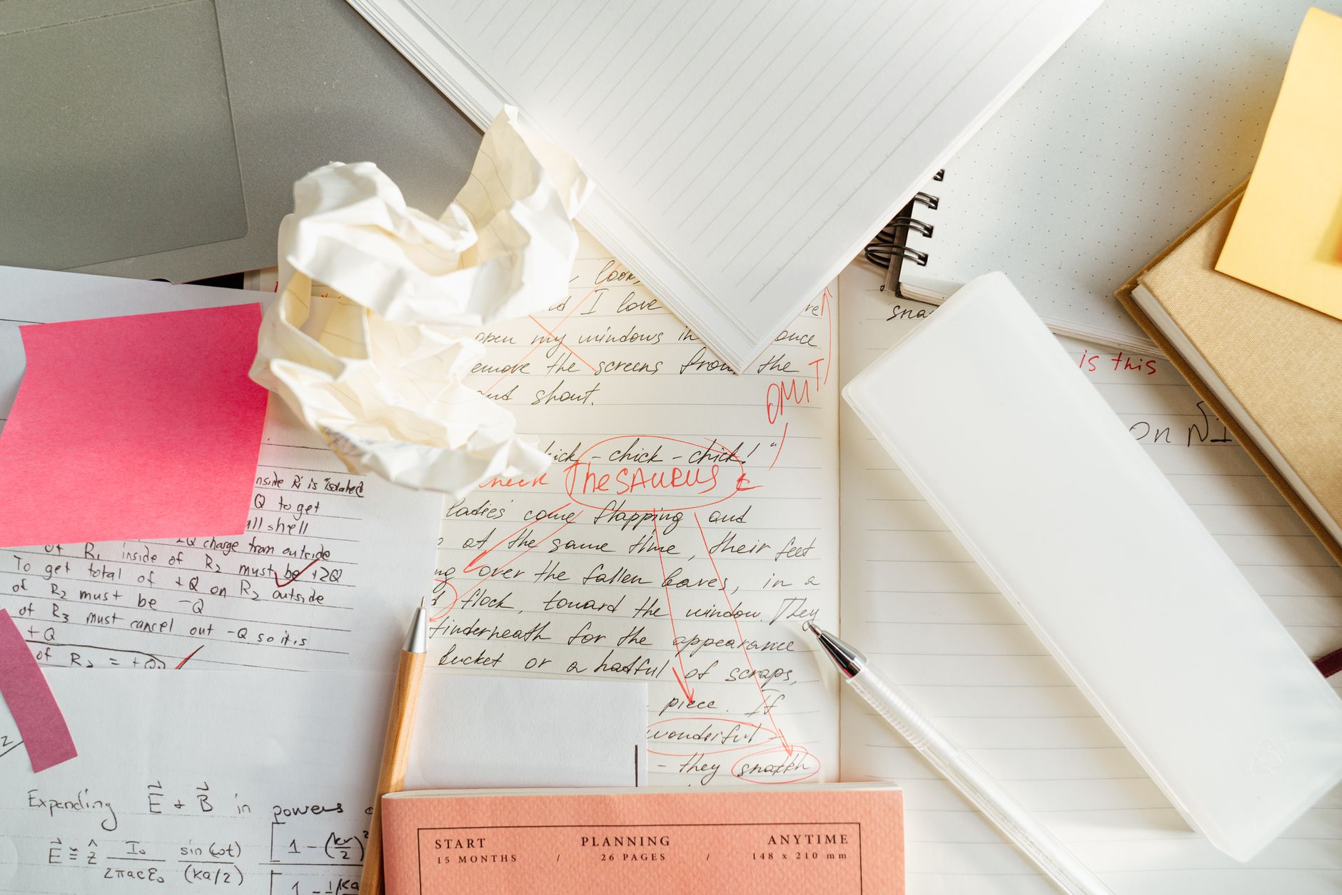 A cluttered workspace with crumpled paper, notebooks, and pens depicting creative chaos.