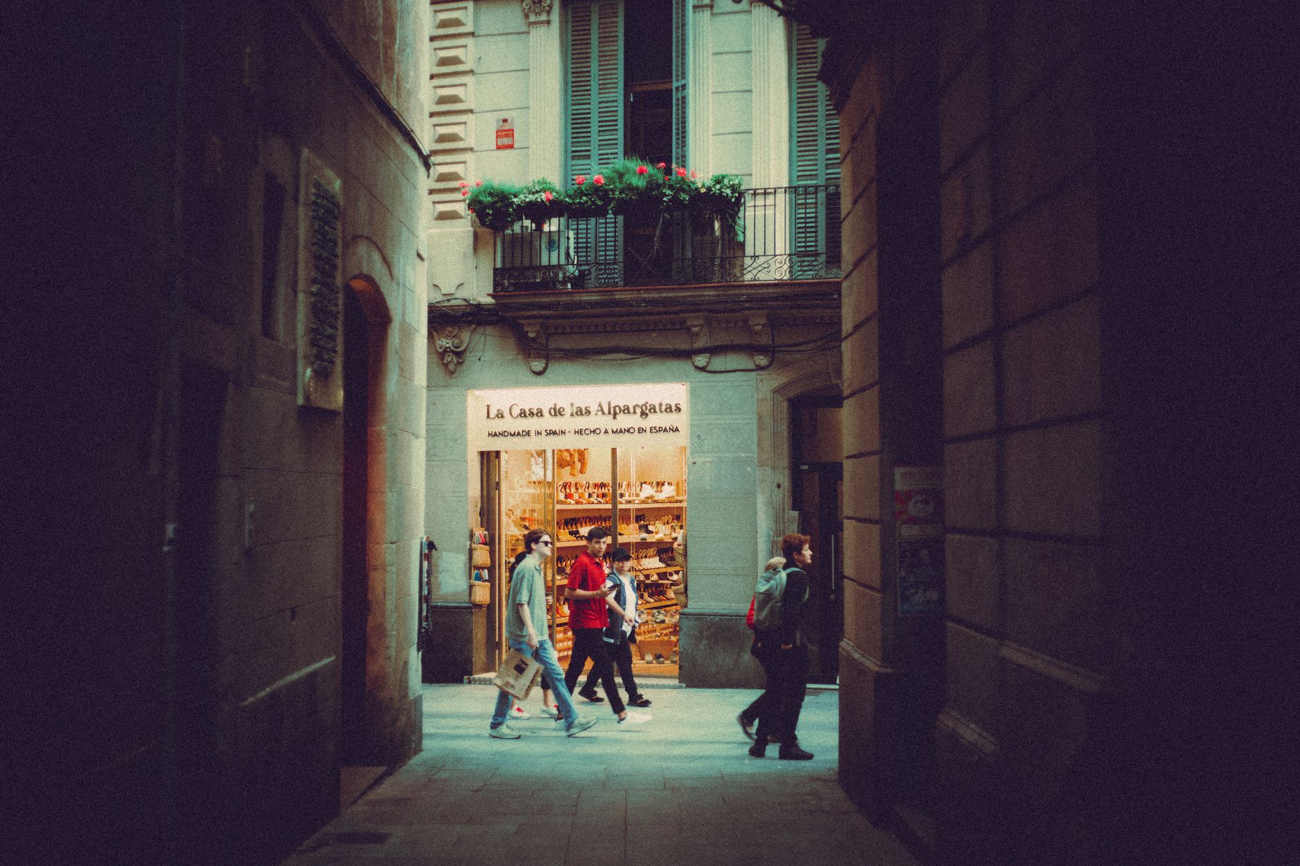 People walking through an alley with a view of a shop front in a historical urban setting.