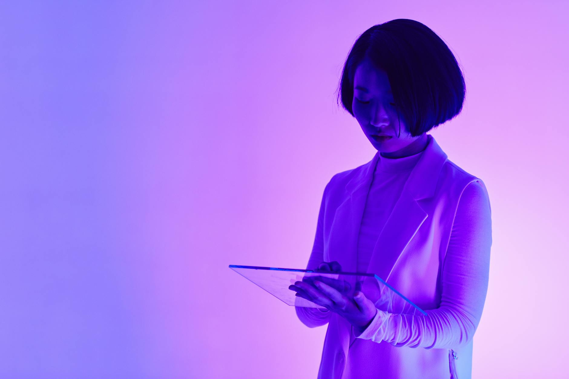A futuristic and conceptual portrait of a woman using a digital tablet in neon lighting.