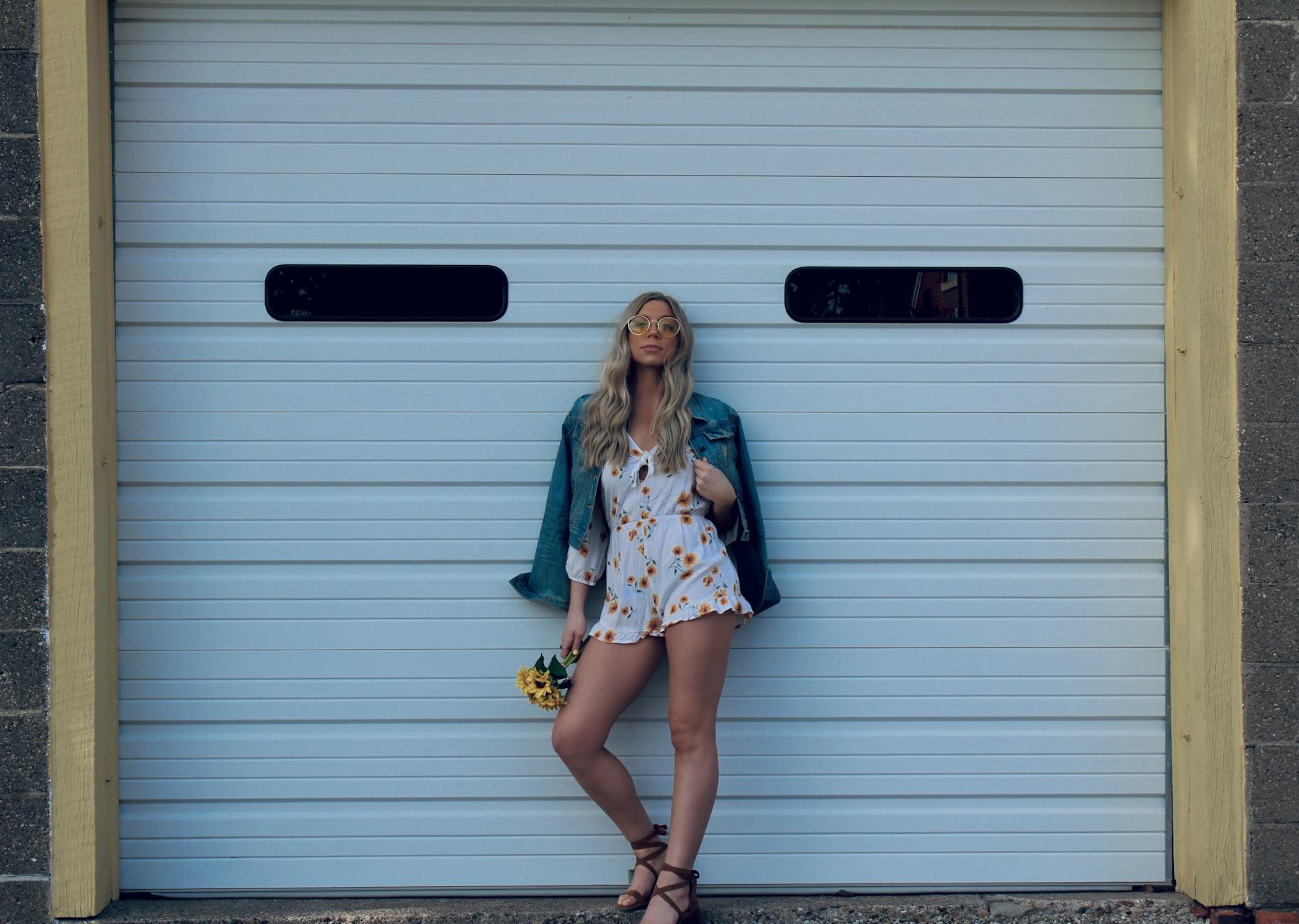 Stylish woman in sunglasses posing against a white garage door in Asbury, IA.
