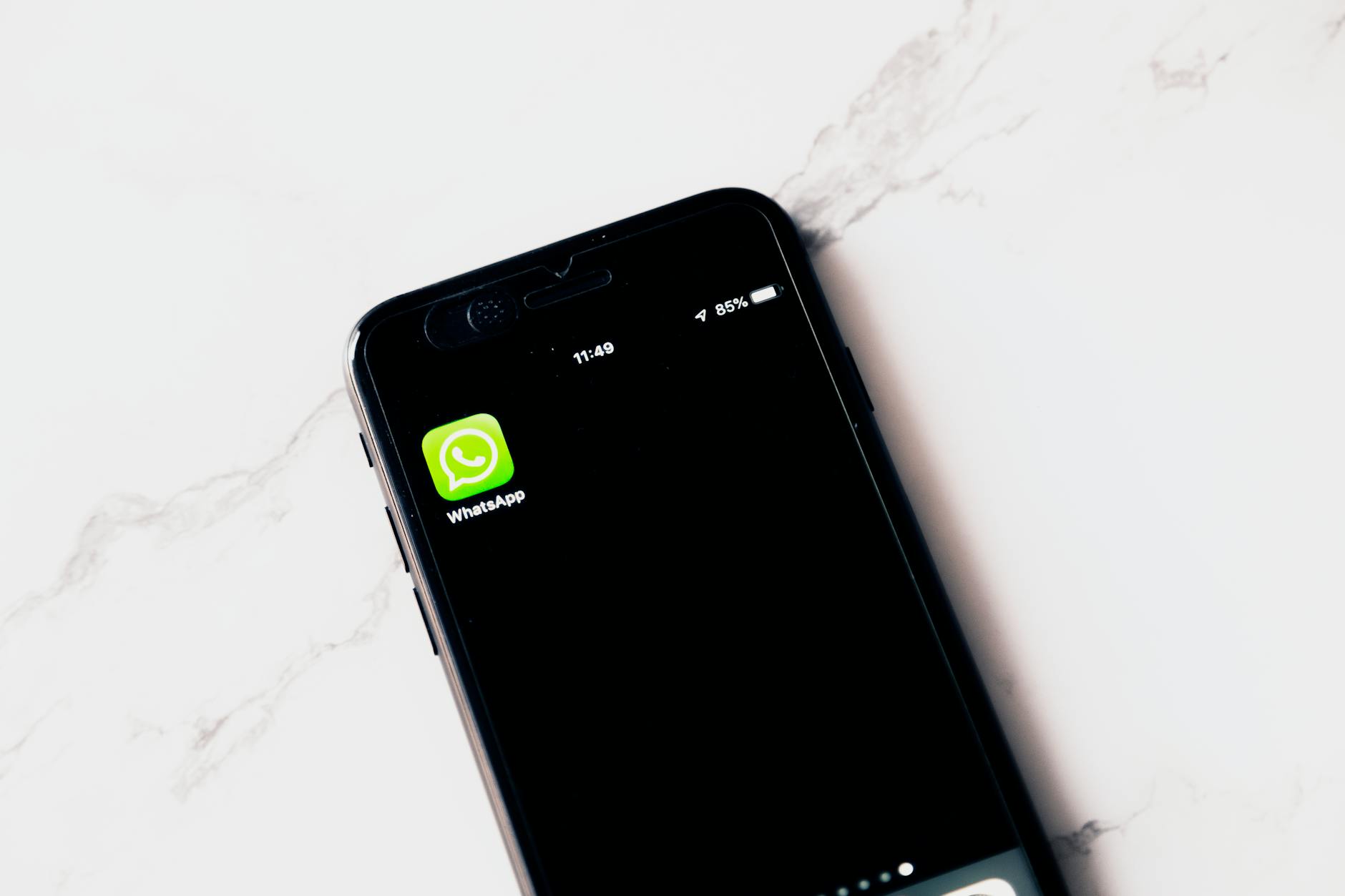 Close-up image of a smartphone displaying WhatsApp on a white table.
